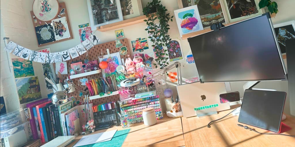 Lilit’s desk with a Kickstarter-stickered laptop, monitor, markers, and wall art